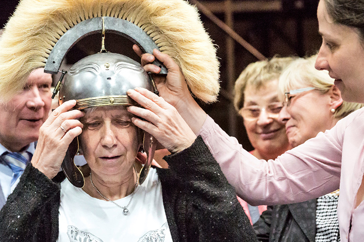 Eine Museumsbesuchern setzt sich einen Helm aus einer Ausstellung auf den Kopf