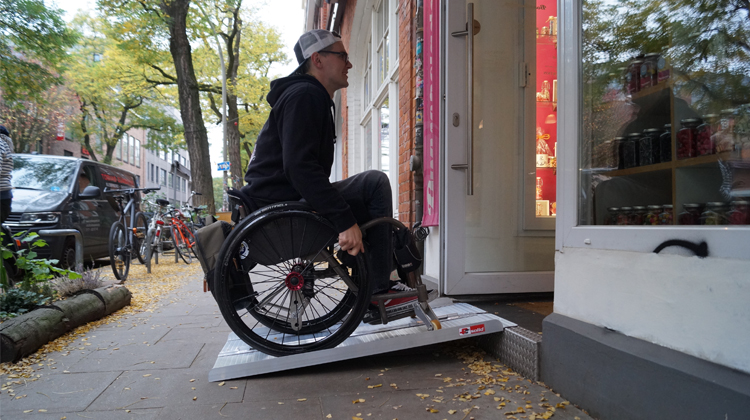 David Lebuser fährt mit dem Rollstuhl auf einer Rampe in ein Geschäft